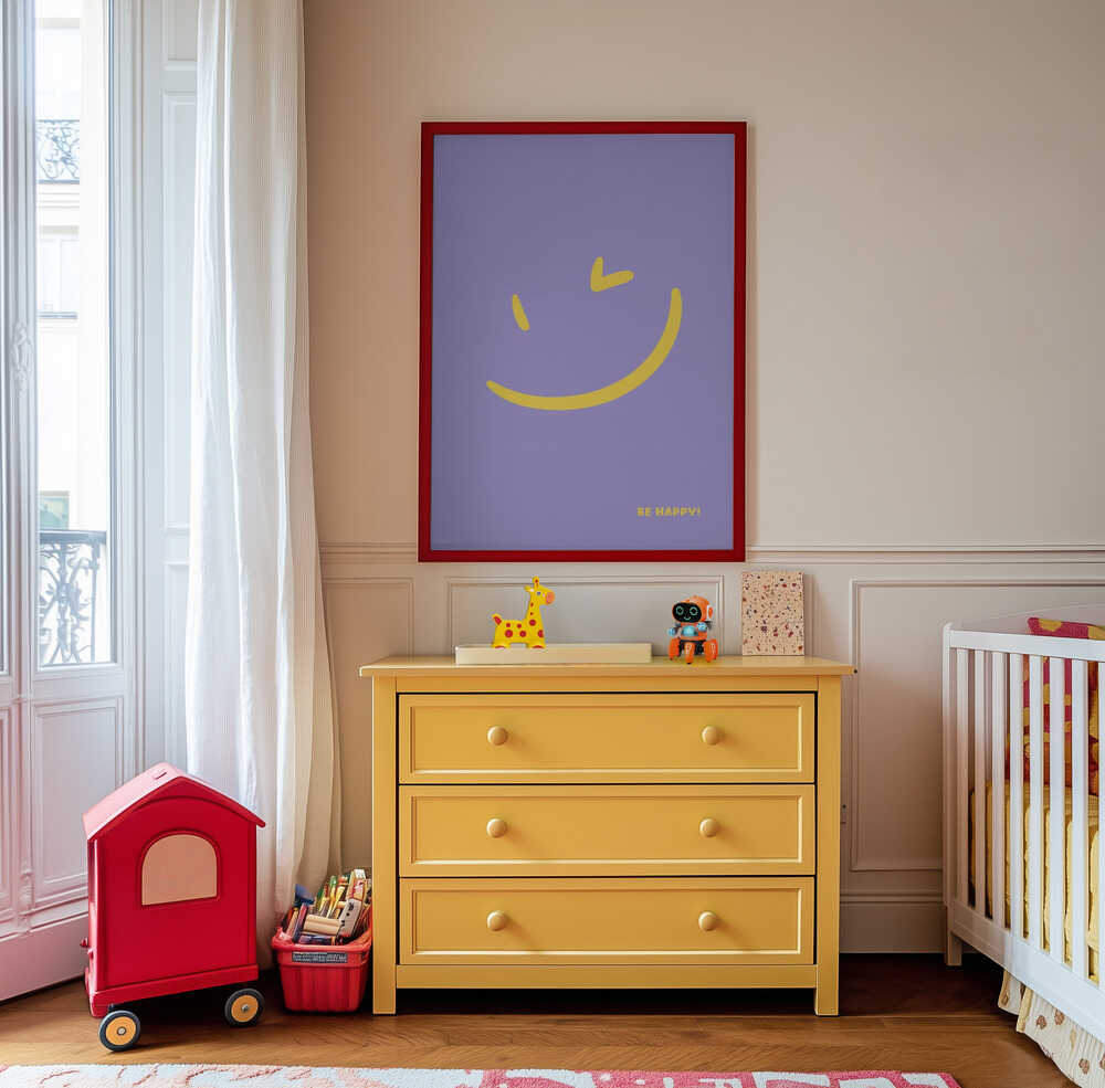 Framed poster with a yellow smiley on a purple background and the text 'Be happy!' written on it. Hanging on the wall above a yellow chest of drawers.