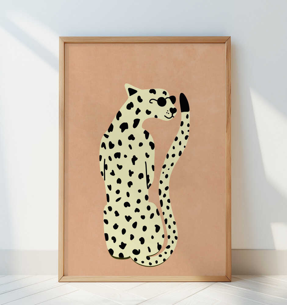 Art print featuring a stylized beige and black leopard on a sand-colored background, displayed in a light wooden frame leaning casually against a white wall with soft natural light.