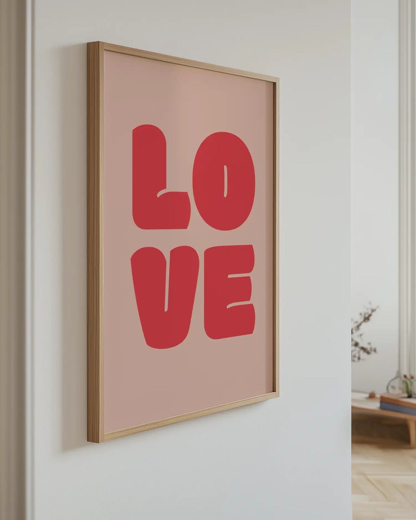 Framed artwork with 'LOVE' in red letters on a light pink background, hanging on a wall.