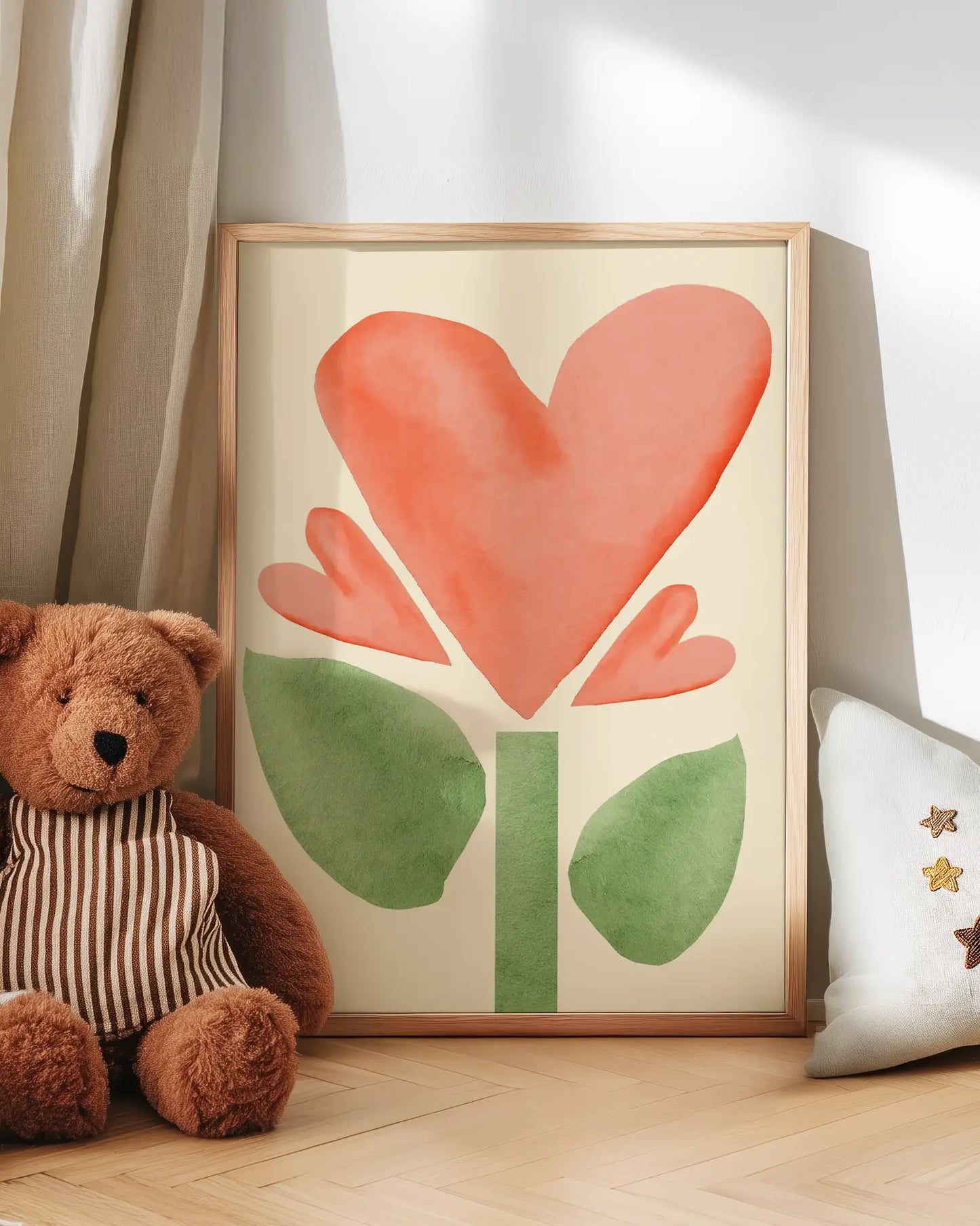 Framed artwork of a pink flower with green leaves on a wooden floor next to a teddy bear and a pillow.