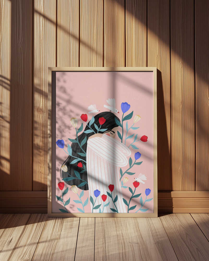 Emotive art print of a woman surrounded by colorful flowers on a soft pink background. Displayed in a light wooden frame leaning against a wooden wall with warm sunlight and shadows. Modern motherhood wall art for Scandinavian interior decor.